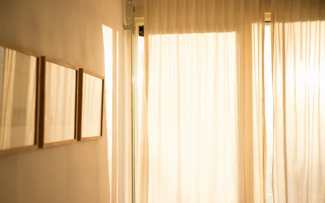 Una habitación clara con cortinas de lino y la luz de la mañana atravesándolas.