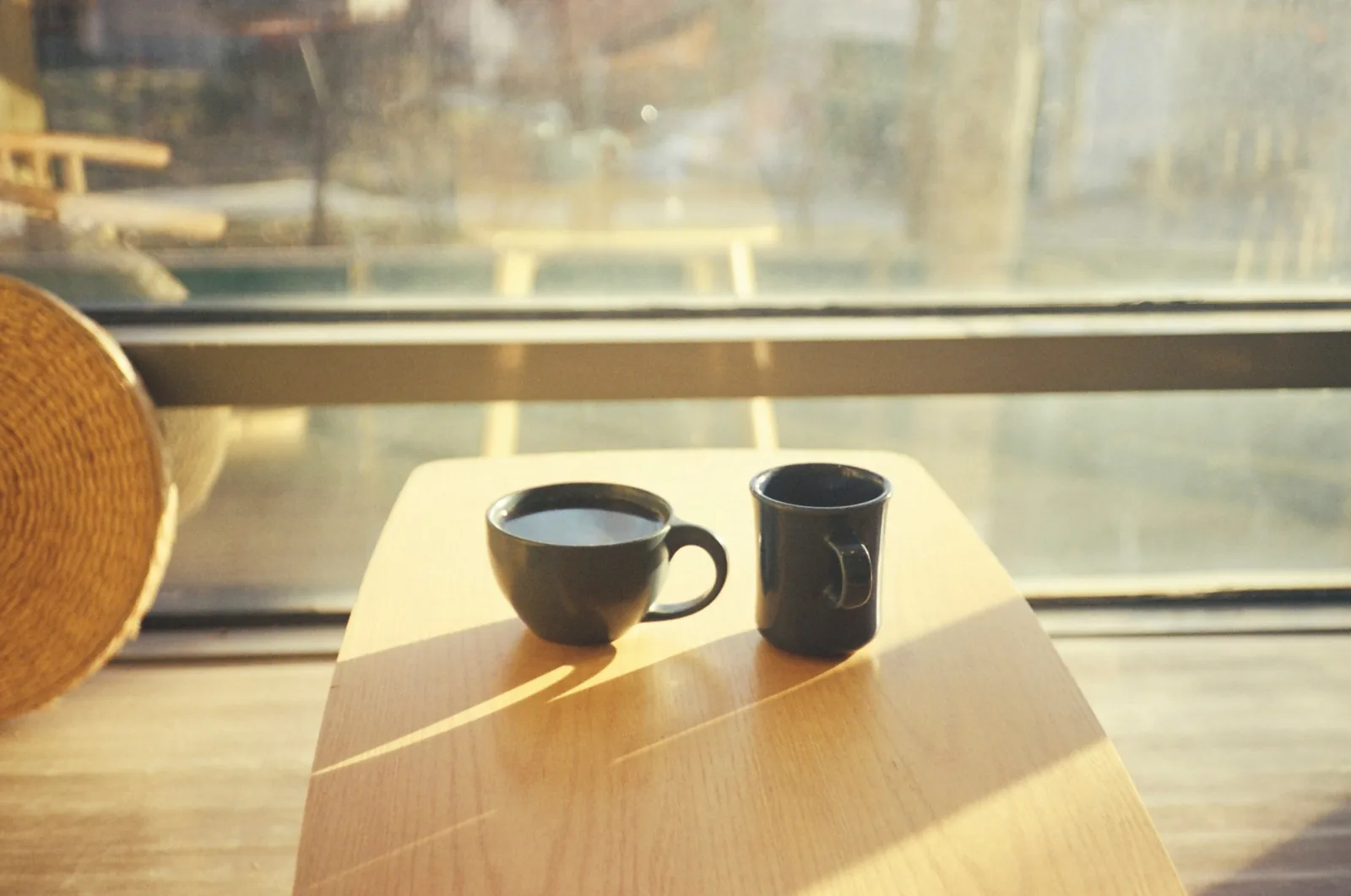 Dos tazas sobre una mesa de madera junto a una ventana, con la luz dorada de la tarde entrando de frente.